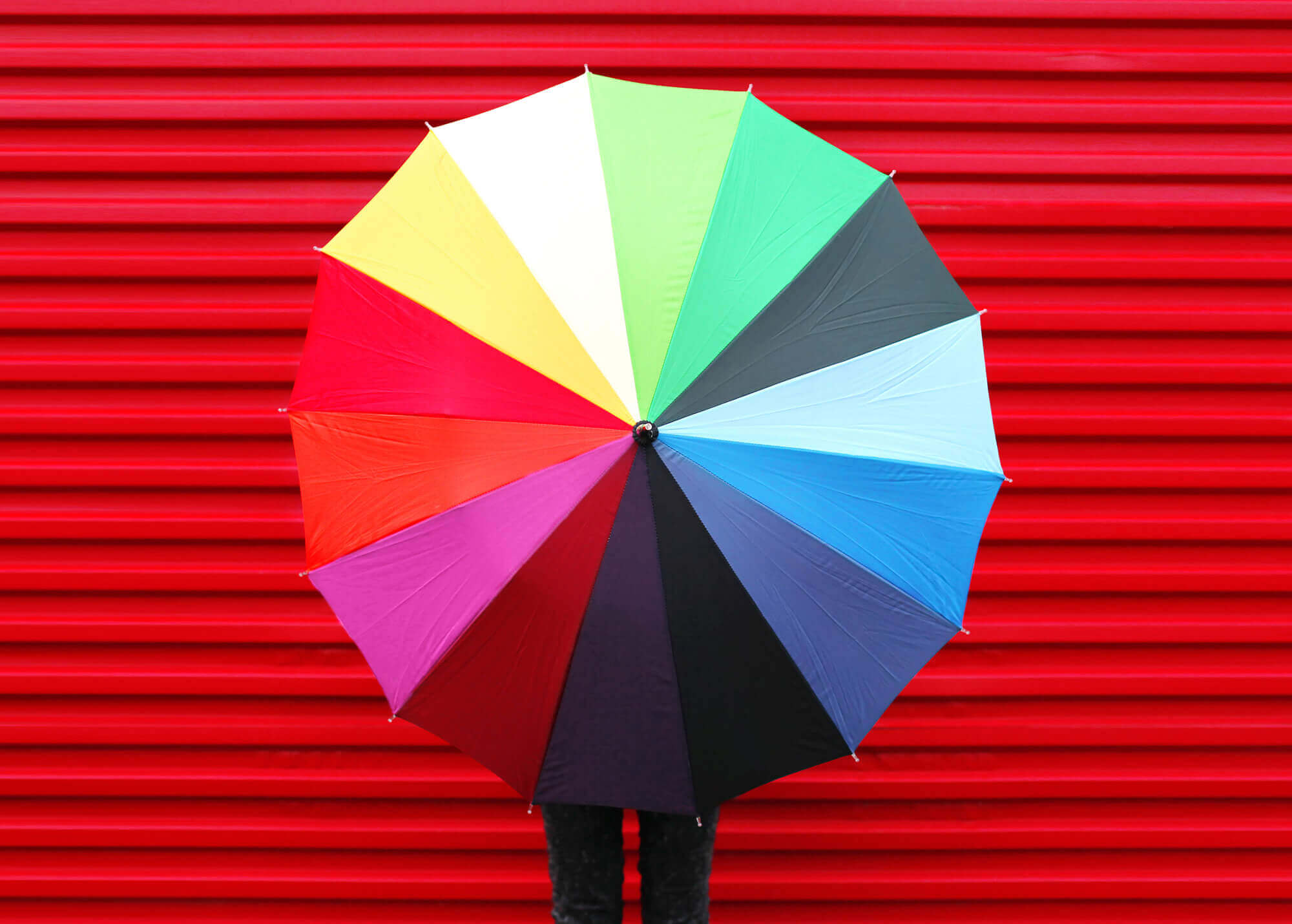 A person holding an umbrella in front of a red wall.