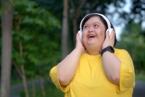 Girl with Down syndrome exercising in the park wearing headphones and a bright yellow t-shirt. Listening to a podcast about the NDIS Reforms