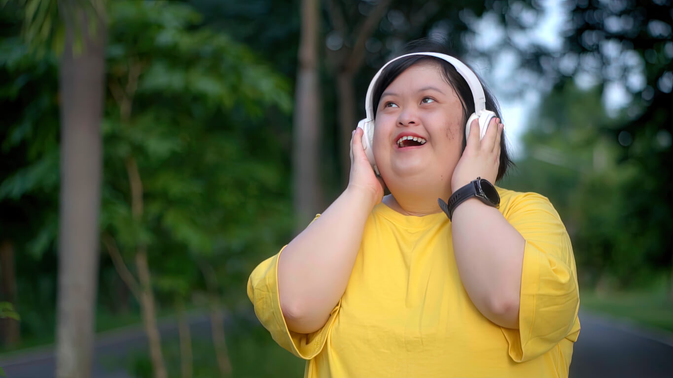 Girl with Down syndrome exercising in the park wearing headphones and a bright yellow t-shirt. Listening to a podcast about the NDIS Reforms